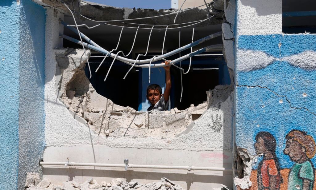 A boy looks through the wall of a building damaged by an Israeli strike at the Abu Hussein U.N. school in the Jebaliya refugee camp in the northern Gaza Strip on Wednesday, July 30, 2014. Israeli tank shells slammed into a crowded U.N. school Wednesday sheltering Gazans displaced by fighting, killing more than a dozen and wounding tens after tearing through the walls of two classrooms, a spokesman for a U.N. aid agency and a health official said. The Israeli military said mortar shells had been fired from near the school, and that soldiers fired back. (AP Photo/Hatem Moussa)